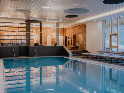 Moderner Innenpool mit Holzdecke, Ruheliegen und großen Fenstern, helle, warme Atmosphäre.