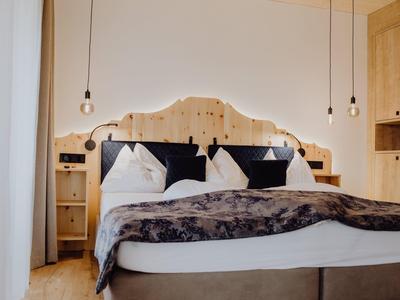 Gemütliches Doppelbett mit Holzkopfteil, weißen Kissen und hängenden Glühbirnen als Beleuchtung.