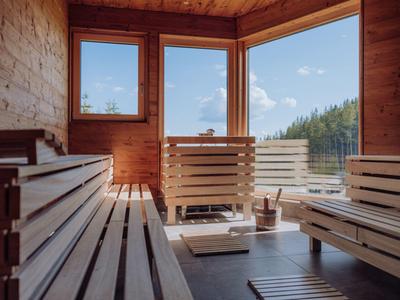 Innenraum einer finnischen Sauna mit Holzbänken, Fensterblick auf blaue Himmel und Wälder.