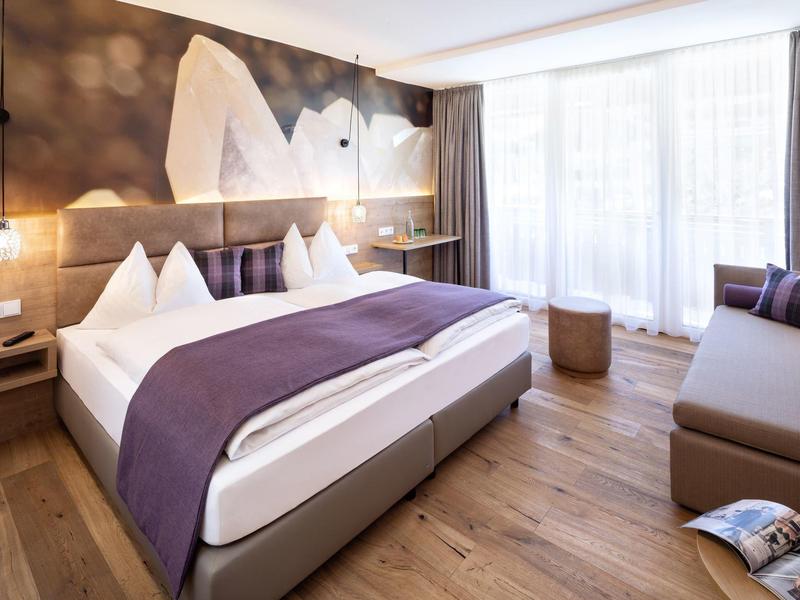 Modernes Schlafzimmer mit großem Bett, lila Decke, Holzfußboden und großem Fenster mit Vorhängen.