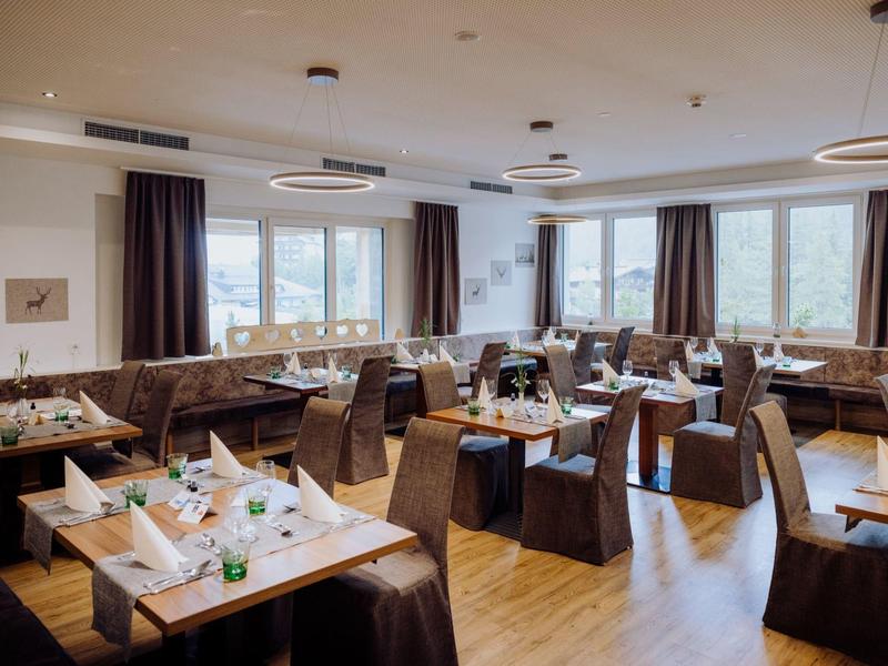 Hell eingerichteter Speisesaal mit Holztischen, bequemen Stühlen und großen Fenstern.