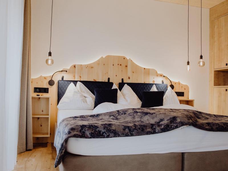 Gemütliches Doppelbett mit Holzkopfteil, weißen Kissen und hängenden Glühbirnen als Beleuchtung.