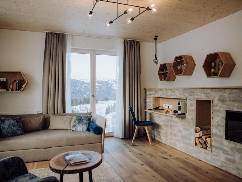 Gemütliches Wohnzimmer mit Sandfarbener Couch, Holzregalen, Kamin und großem Fenster mit Vorhängen.