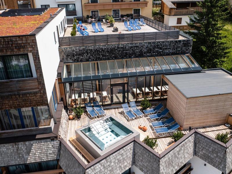 Moderne Dachterrasse mit Holzbelag, Whirlpool, Sitzgruppen und Glasgeländer in sonnigem Umfeld.
