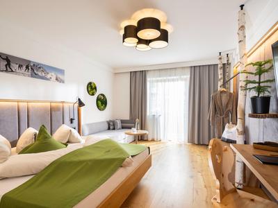 Modern hotel room with a double bed, green accents, large window, and wooden furniture.