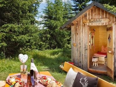 Gemütliche Picknickbank vor einer kleinen Holzhütte im Wald mit Essen und Getränken.