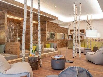 Gemütlicher Lounge-Bereich mit Holzwänden, Birkenstämmen und modernen Sitzmöbeln in einem Hotel.