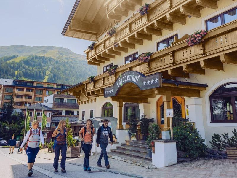 Guests arrive at a mountain hotel with wooden balconies and scenic views.