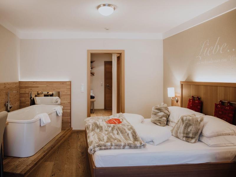 Cozy hotel room with double bed, bathtub, wooden walls, and warm lighting.