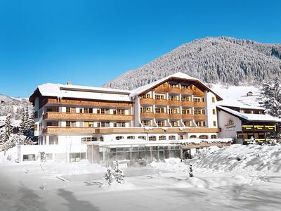 Großes Hotel mit Holzfassade vor schneebedeckten Bergen und blauem Himmel.