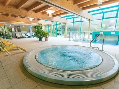 Runder Whirlpool mit blubberndem Wasser in hellem Raum mit großen Fenstern und Holzbalkendecke.