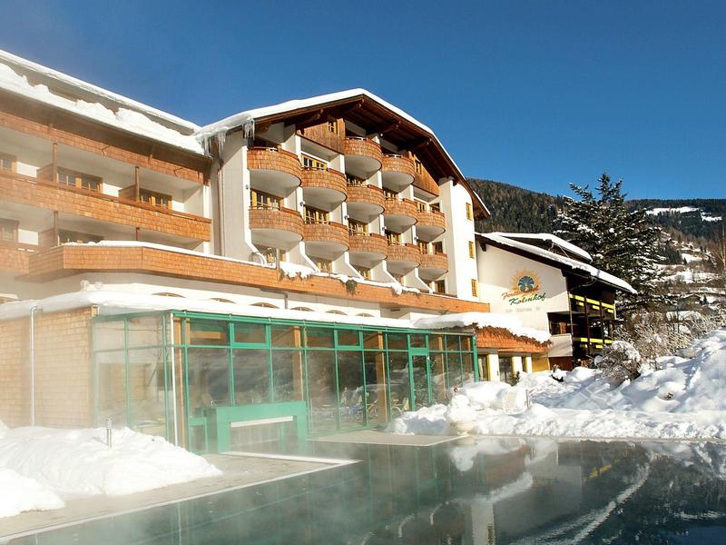 Hotelgebäude mit Balkon, umgeben von Schnee und einem Becken oder Teich davor.