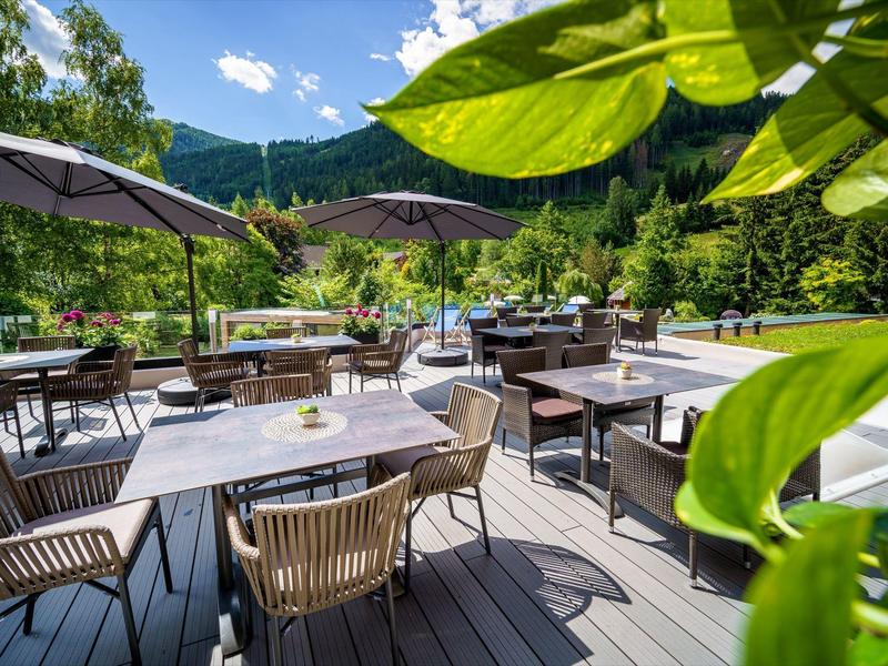 Freiluftterrasse mit Holztischen, Stühlen und großen Sonnenschirmen, umgeben von grüner Natur.