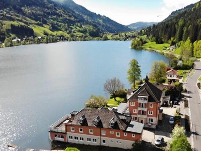Idyllischer Bergsee mit grünen Hängen, Häusern am Ufer und klarer, ruhiger Wasserfläche.