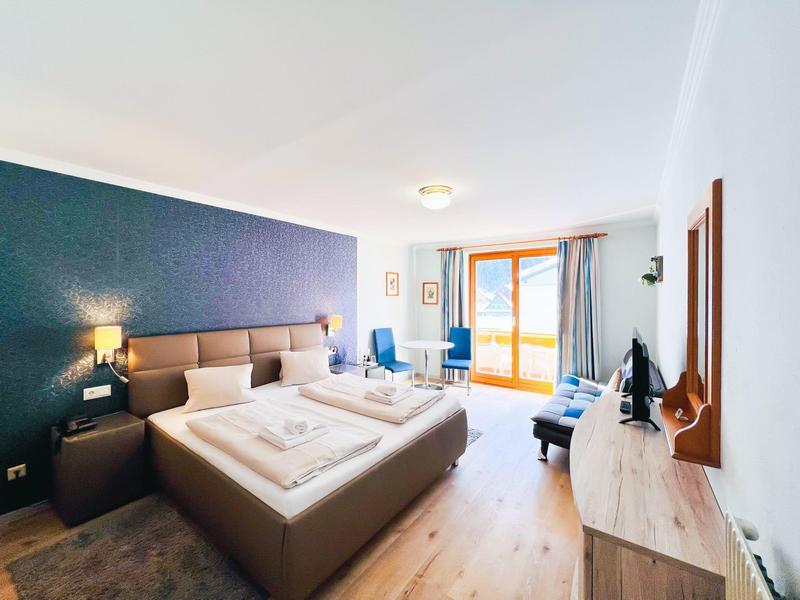 Bright double room with large bed, TV, seating area, and balcony access.