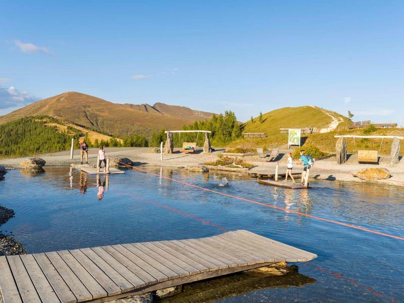 Mountain lake with wooden pier and lounge chairs under clear sky in a holiday resort.