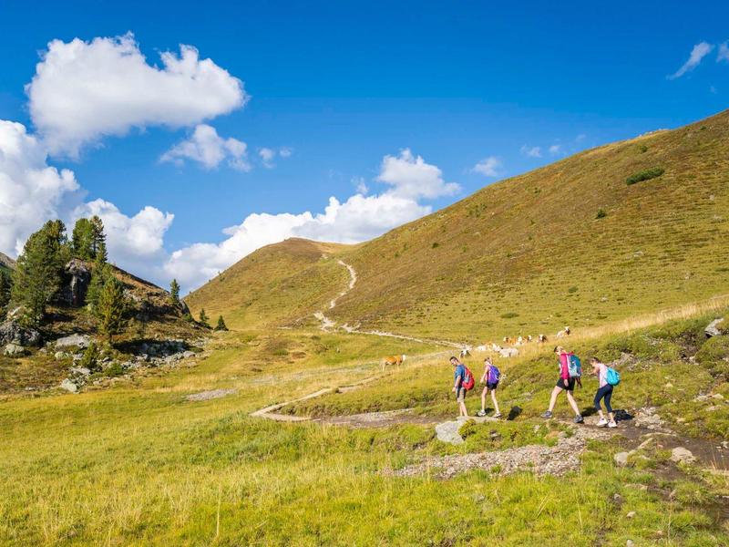 Hikers walk along a trail through green hills under a clear blue sky.