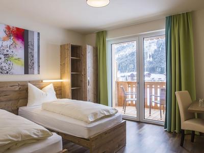 Helles Hotelzimmer mit zwei Einzelbetten, Holzmöbeln und Balkon mit Bergblick.