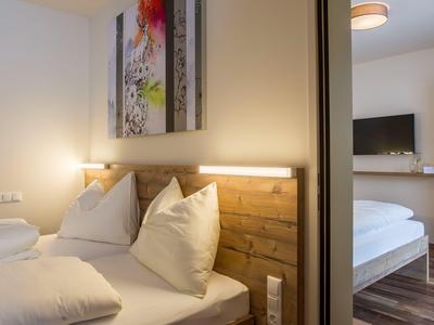 Modernes Hotelzimmer mit zwei Einzelbetten, Holzakzenten und abstraktem Bild über dem Kopfteil.