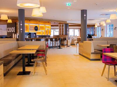 Helles, modernes Restaurant mit bequemen Sitzgelegenheiten und Stehbereich, warm beleuchtet.