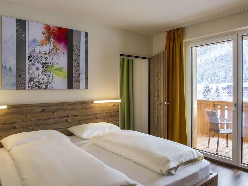 Schlafzimmer mit zwei Einzelbetten, Holzdekor, großem Fenster und Balkon mit Bergblick.