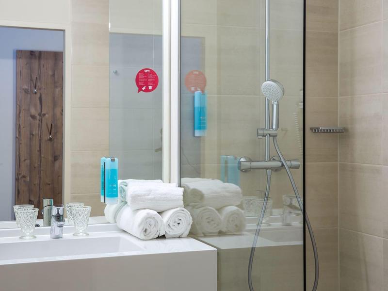 Modernes Badezimmer mit Glasdusche, weißen Handtüchern und blauen Flüssigseifenflaschen.