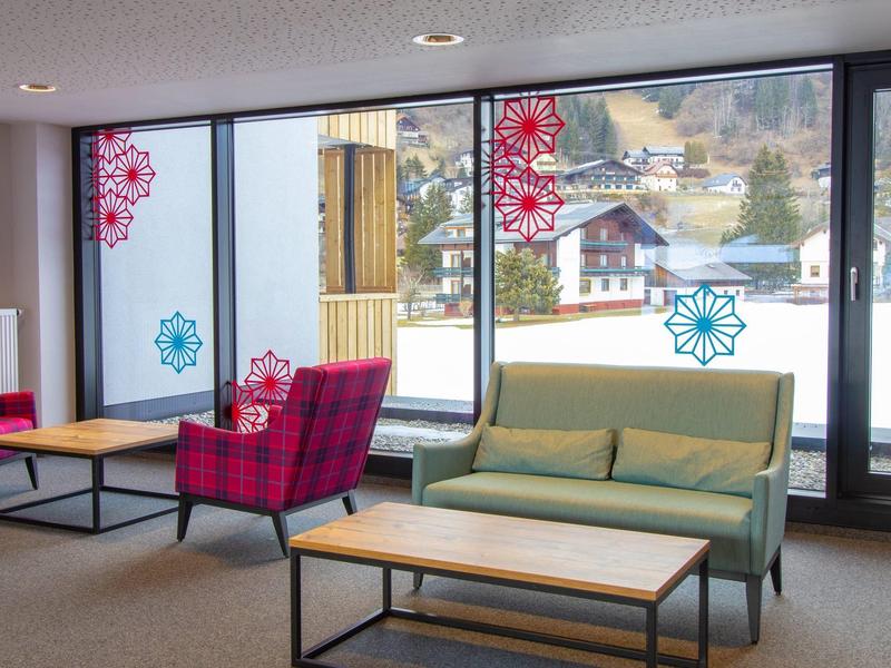 Gemütlicher Sitzbereich mit grünem Sofa, rotem Sessel, Holztischen und dekorativen Fensteraufklebern.