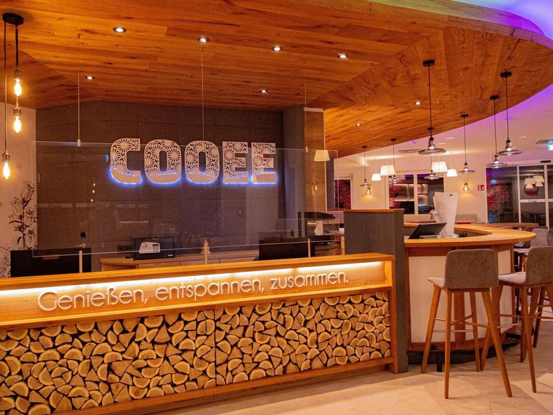 Modernes Café mit warmem Holzdesign, heller Theke und gemütlicher Bar mit hohen Hockern.