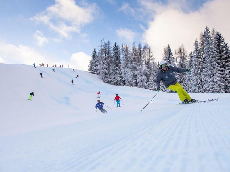 Skifahrer auf einer präparierten Piste mit schneebedeckten Bäumen und blauem Himmel