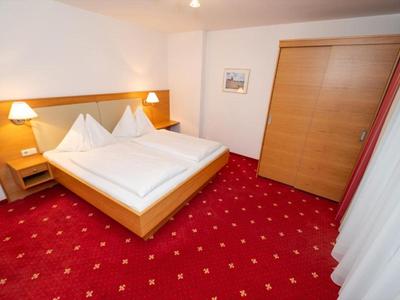 Ein einfach eingerichtetes Hotelzimmer mit Doppelbett, roten Teppichboden und Holzschrank.