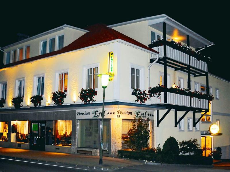 Zweistöckiges weißes Gebäude mit Balkonen, roten Dach und beleuchteten Fenstern bei Nacht.