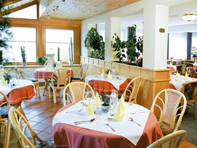 Acogedora zona de restaurante de hotel con muebles de madera y mesas con manteles blancos y rojos.