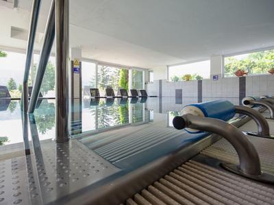 Moderner Innenpool mit Edelstahl-Wasserfontänen und ruhiger Atmosphäre, große Fenster mit Blick ins Grüne.