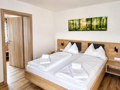 Habitación de hotel moderna con muebles de madera, cama doble, ropa de cama blanca y cuadro de bosque en la pared.
