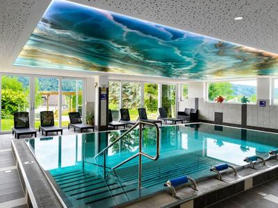 Área de spa moderna con piscina cubierta, grandes ventanales y iluminación colorida en el techo.