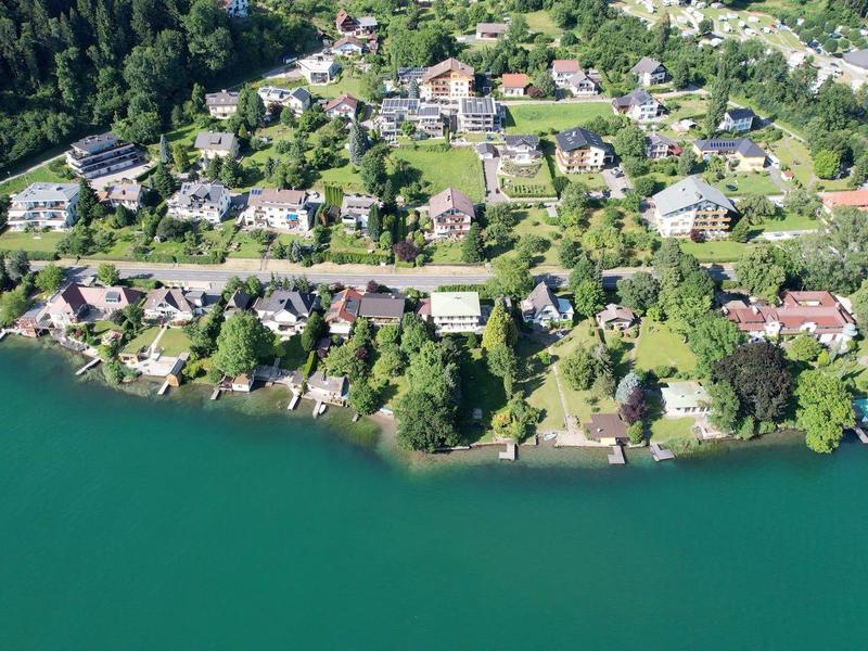 Kleines Dorf mit Häusern am Ufer eines grünen Sees, umgeben von dichtem Wald.