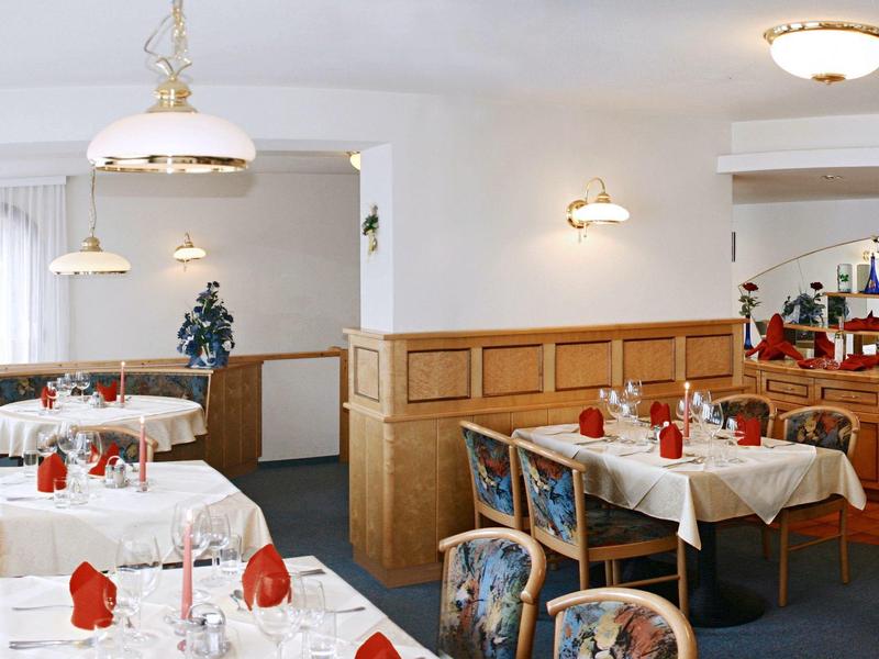 Restaurant mit gedeckten Tischen, weißen Tischdecken und roten Servietten in hellem, freundlichem Raum.