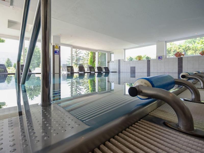 Moderner Innenpool mit Edelstahl-Wasserfontänen und ruhiger Atmosphäre, große Fenster mit Blick ins Grüne.