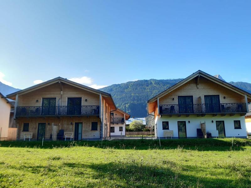 Two adjacent chalet houses in front of a mountain landscape under clear sky.