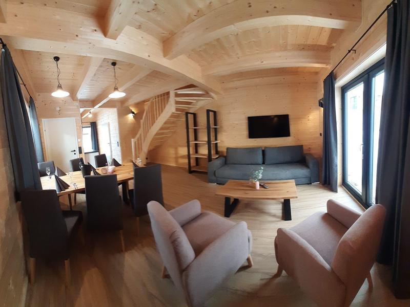 Living room with wooden ceiling, sofa, armchairs, coffee table, and TV near large windows.