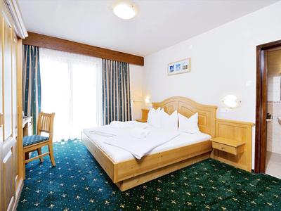 Helles Hotelzimmer mit Doppelbett, grünem Teppich und Zugang zum Badezimmer.