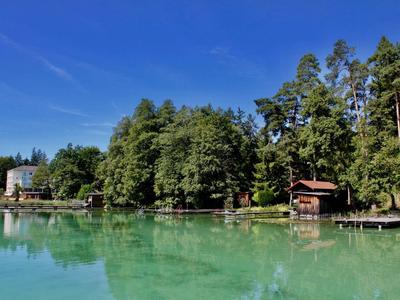 Klarer See mit smaragdgrünem Wasser und bewaldetem Ufer unter blauem Himmel.