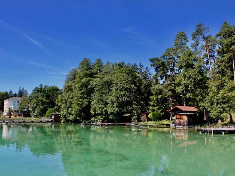 Ufer mit Bäumen, Bootshaus und Häusern an einem ruhigen, klaren See