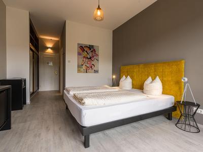 Modernes Hotelzimmer mit Doppelbett, gelb gepolstertem Kopfteil und minimalistischer Einrichtung.