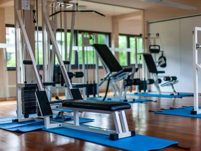 Heller Fitnessraum mit verschiedenen Trainingsgeräten und blauen Matten auf Holzboden.