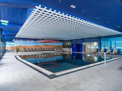 Moderner Innenpool mit blauer Decke, großen Fenstern und Entspannungsbereichen.