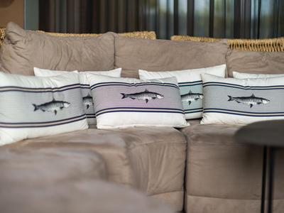Drei dekorative Kissen mit Fischmotiven auf einem beigen Sofa in einem Wohnzimmer.