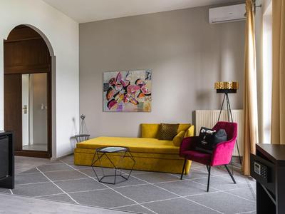 Modern eingerichtetes Wohnzimmer mit gelbem Sofa und pinkem Sessel, helle Vorhänge und Wandkunst.