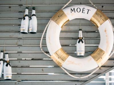 Rettungsring mit der Aufschrift Moët und Champagnerflaschen an einer Holzverkleidung.