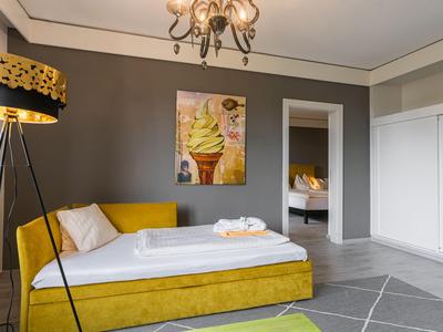 Modernes Hotelzimmer mit gelbem Sofa, Teppich und Wandbild, Blick ins Schlafzimmer.